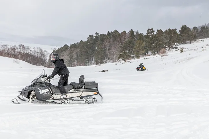 A rider standing on a snowmobile with a cargo sled in a snowy field.