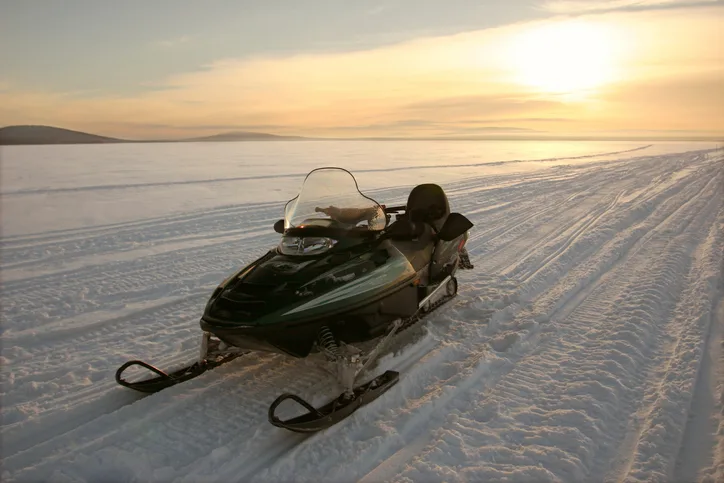 A snowmobile parked on a snowy plain at sunset.
