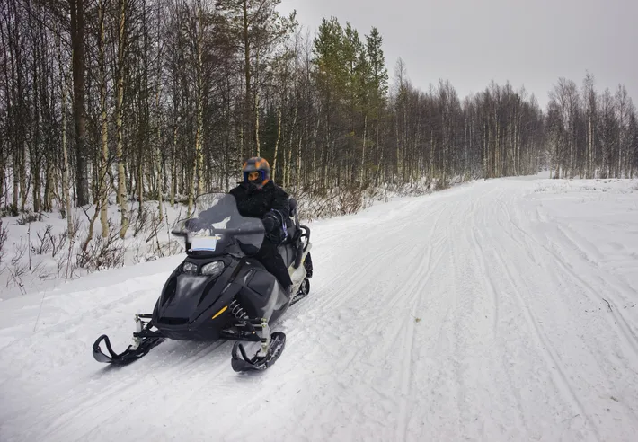 Förare på snöskoter på en snötäckt skogsväg.